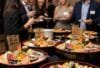Ein professionell aufgebautes Catering-Buffet bei einem Firmenevent. Im Fokus stehen mehrere große, kunstvoll arrangierte Sushi-Platten von Itoshii. Im Hintergrund sind zufriedene Gäste im Gespräch.
